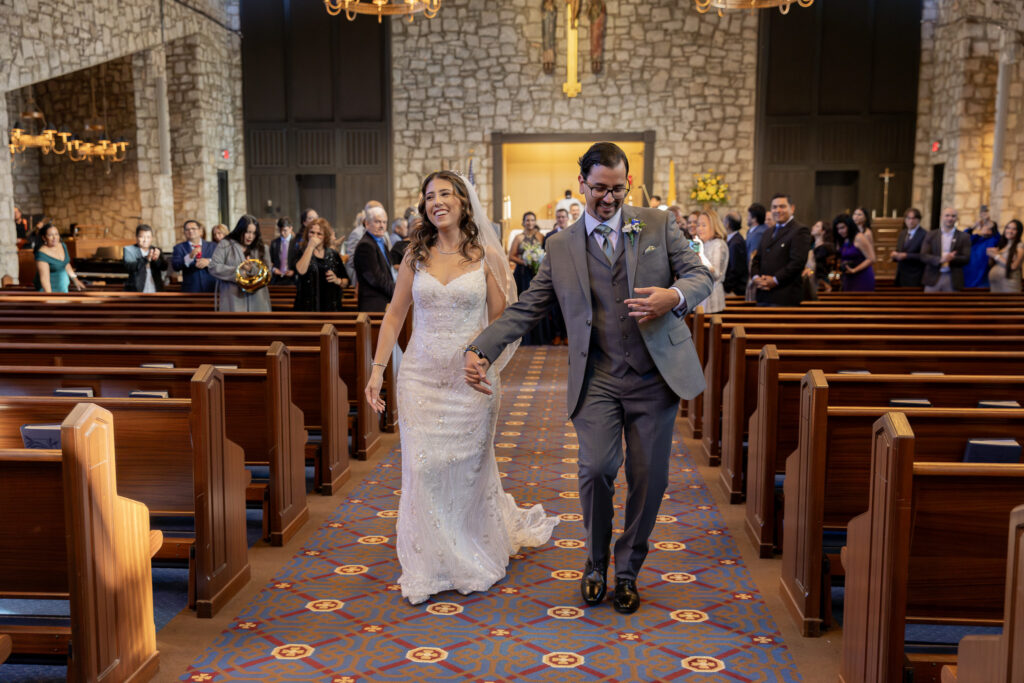 The bride and groom walking down the aisle after the ceremony ends, and the groom is doing a fun little dance.