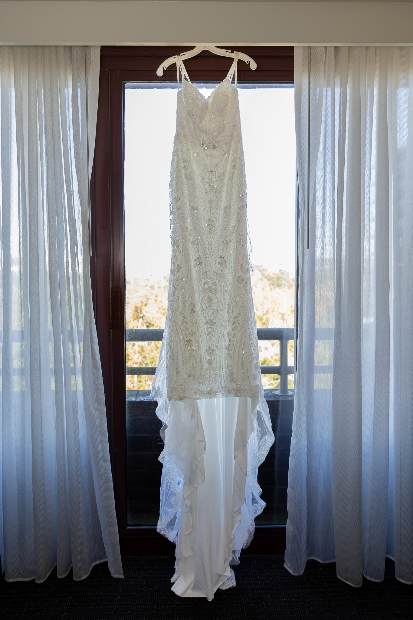 Wedding dress hanging in front of glowing window.