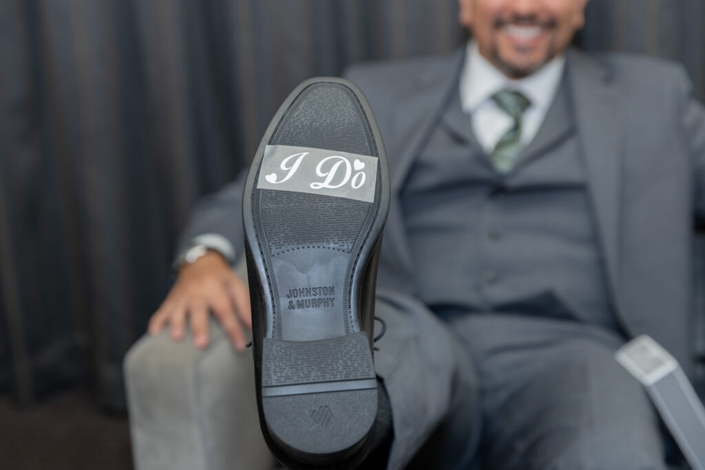 The letters I Do are stickered on the bottom of the groom's shoes.