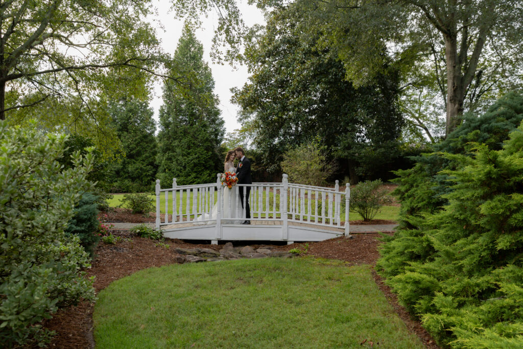 A portrait of the bride and groom on a cute small bridge with trees and greenery surrounding them.