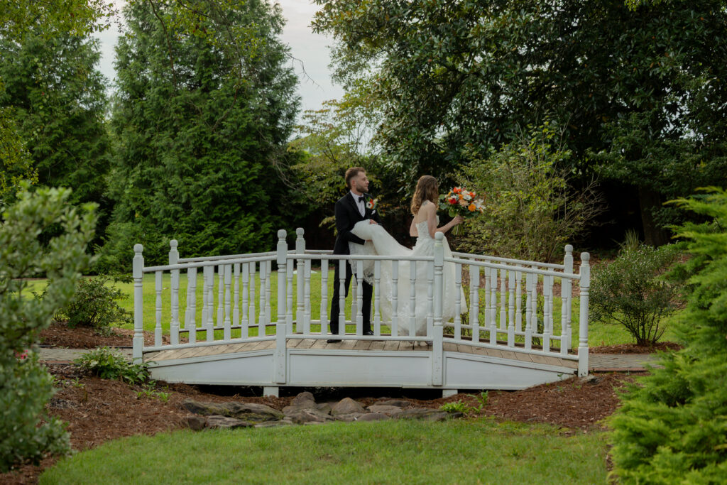 The groom holding the back of the bride's dress as she walks across the bridge.