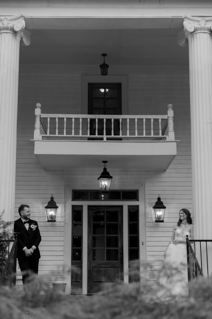 The bride and groom on their wedding day each leaning on a column pillar looking at one another smiling.